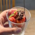 En hand som håller ett glas med jordgubbar och en bit brownie i en sked.