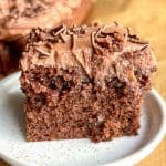 Bit av chokladkaka med chokladglasyr och strössel på en vit tallrik.