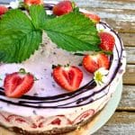 Glasstårta dekorerad med jordgubbar, blad och chokladlinjer på toppen.