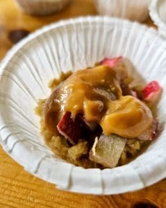 Havrekaka med bitar av rabarber och en sked dulce de leche på toppen i en pappersskål.