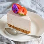 En bit cheesecake med jordgubbar och rabarber på en vit tallrik med en sked.