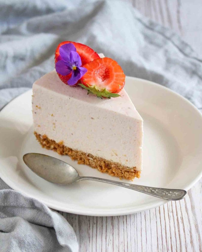 Smulpaj med rabarber och jordgubbar 11 En bit cheesecake med jordgubbar och rabarber på en vit tallrik med en sked.