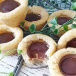 Kakor med en rund chokladfyllning i mitten, placerade på en yta med gröna växter.