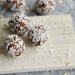 Tre chokladbollar rullade i kokosflingor på en träskärbräda.