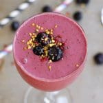 Bärsmoothie i ett glas med blåbär och frön på toppen, serverad med sugrör.