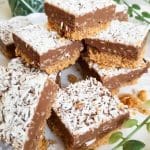 Nougat- och kokosrutor staplade på en tallrik, med kokosflingor på toppen.