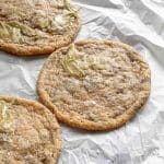 Tre pistagecookies placerade på ett bakplåtspapper med en smörig yta.